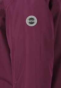 Lilla stof med en glat tekstur har et rundt gråt logo-mærke med "ZIGZAG" og teksten "UDFORSKER AKTIV LIVSSTIL UDE."