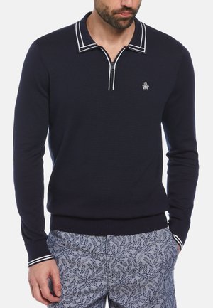 Pull en marine avec col zippé et détails à rayures blanches. Présente un petit logo brodé sur la poitrine. Fabriqué en tissu tricoté.