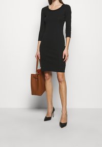 Svart figursydd klänning med rundad halsringning och trekvartslånga ärmar, kombinerad med spetsiga svarta klackar och en beige handväska.