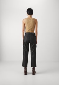 Beige ribbet topp kombinert med svarte cargo-bukser med sidelommer. Modellen har på seg brune hæler, med kort mørkt hår.