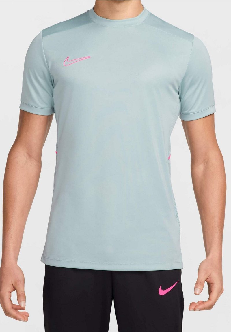 Vaaleansininen urheilupaita, joka on valmistettu sileästä kankaasta, jossa on lyhyet hihat ja vaaleanpunaiset Nike-logot rinnassa ja sivuilla.