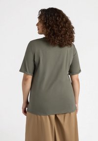 Camisa de manga corta en verde oliva, hecha de un material suave y con un corte relajado, que presenta mangas enrolladas y un dobladillo curvado.
