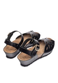 Sandales noires avec un design découpé en forme de feuille, sangle ajustable avec boucle dorée, semelle en liège et semelle texturée noire.
