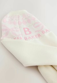Suave suéter de punto blanco con patrones geométricos y letras en rosa, que incluye una prominente "B" y el texto "BAKER" en la zona del cuello.