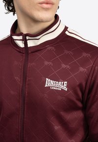 Bordo zip-up jakna s rebrastim ovratnikom, s quiltanim uzorkom i suptilnim grafikom lava, te Lonsdale London logom u bijeloj boji.