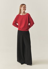 Pull en maille rouge avec un large décolleté, associé à un pantalon noir ample avec une fente à l'avant. Texture douce et coupe décontractée.