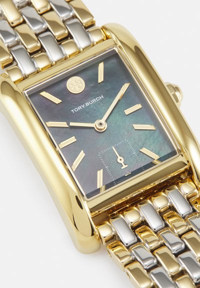Montre bracelet à maillons dorés et argentés avec cadran noir rectangulaire, index dorés, aiguilles et logo Tory Burch à 12 heures.
