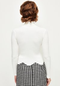 Pull blanc côtelé avec un col montant et un ourlet festonné, associé à une jupe pied-de-poule noir et blanc. Texture lisse, silhouette ajustée.