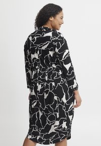 Vestido de patrón en blanco y negro con mangas largas, cintura elástica y aberturas laterales. Tejido suave con una caída fluida, que presenta un diseño abstracto.