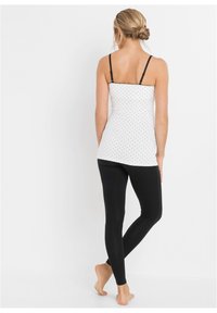 Top bianco senza maniche con pois neri, spalline sottili nere, abbinato a leggings neri. Il tessuto è liscio, creando una silhouette aderente.