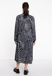 Langes, schwarz-graues gestreiftes Kleid mit plissierter Textur, langen Ärmeln und geradem Schnitt, kombiniert mit schwarzen Plateauschuhen.