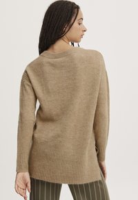 Pull en maille beige clair, avec un ourlet et des poignets côtelés, au fit ample et au design à épaule tombante, idéal pour superposer.