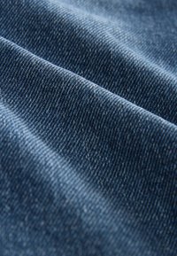 Material denim de culoare albastru închis, cu o suprafață texturată ce prezintă modele diagonale de țesătură și variații ușoare de nuanță.