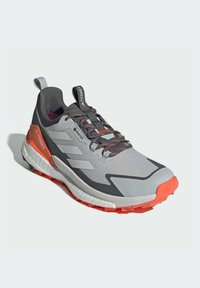 Buty biegowe Gore-Tex, szare z pomarańczowymi akcentami, teksturowana cholewka, sznurowany design, wytrzymała podeszwa oraz wyraźny uchwyt na pięcie dla łatwego zakładania.