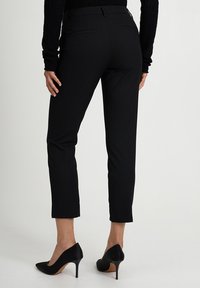 Pantaloni neri su misura con una vestibilit9 slim, dotati di tasche laterali e orlo pulito. Abbinati a scarpe con tacco alto nere, che mostrano una trama liscia.