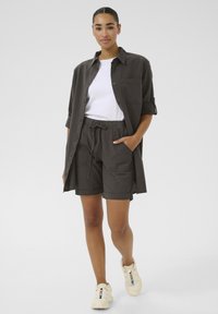 Chemise en lin grise et shorts assortis, coupe décontractée avec des manches retroussées, associés à un t-shirt blanc et des baskets beiges. Texture lisse.