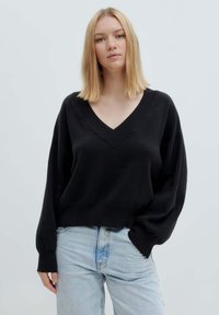 Schwarzer gestrickter Pullover mit tiefem V-Ausschnitt, oversized Ärmeln und lockerer Passform, kombiniert mit hellblauen Jeans.