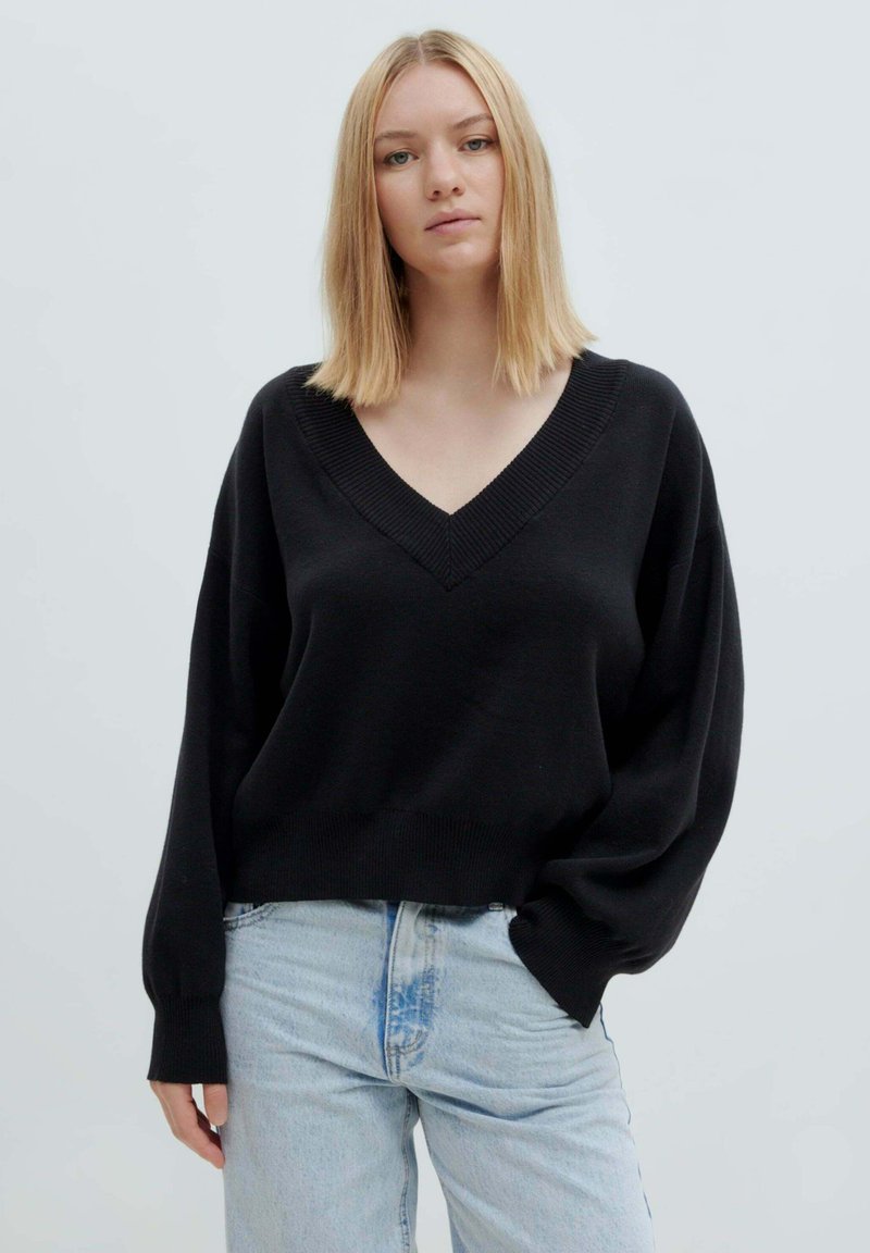 Schwarzer gestrickter Pullover mit tiefem V-Ausschnitt, oversized Ärmeln und lockerer Passform, kombiniert mit hellblauen Jeans.