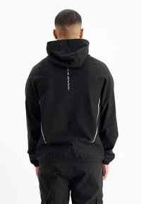 Zwarte hooded jack met verstelbare capuchon, elastische manchetten en reflecterende accenten. Heeft een ruime pasvorm en een soepele textuur.