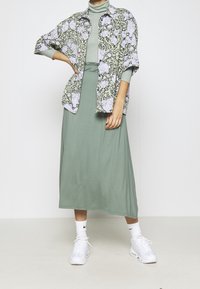 Lyhythihainen kukkakuosisarja vaaleissa väreissä vihreän polvipituisen mekon päällä. Yhdistettynä valkoisiin tennareihin ja nilkkasukkiin.