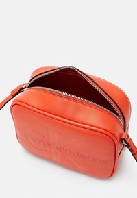 Borsa a tracolla Calvin Klein Jeans in pelle arancione brillante. Forma rettangolare con logo impresso, chiusura con zip superiore e tracolla regolabile.