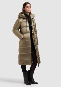 Geacă lungă, cu glugă, din material pufos, de culoare verde metalizat, cu panouri matlasate, buzunare frontale, șnururi de ajustare și un design până la genunchi.