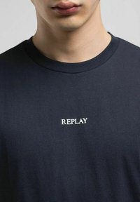 T-shirt in cotone blu navy con scollatura a girocollo, caratterizzato da un logo "REPLAY" ricamato sul petto. Tessuto morbido, design aderente.