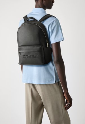 Black leather backpack with a textured finish, featuring a front zip pocket, adjustable straps, and embossed brand logo detail.