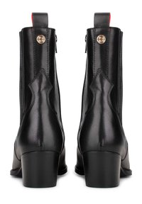 Botas de cuero negro hasta el tobillo con tacón cuadrado, cremallera trasera, herrajes en tono dorado y acentos rojos decorativos en la lengüeta y el detalle lateral.