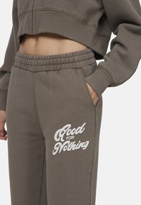 Felpa grigia tagliata con polsini a coste, abbinata a pantaloni jogger grigi con vita elasticizzata e stampa bianca "Good for Nothing" sulla coscia.