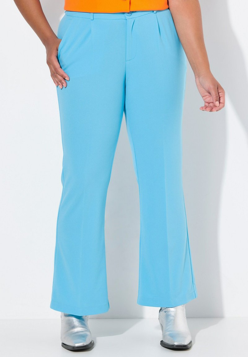 Pantalons évasés bleu clair avec une texture lisse, dotés de poches sur les côtés et d'une taille simple. Portés avec des bottes argentées brillantes.