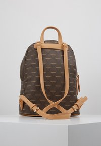 Mochila castanha com padrão, com detalhes em couro beije, alças ajustáveis, pega no topo e um bolso lateral com fecho. Apresenta um design de logotipo repetido.