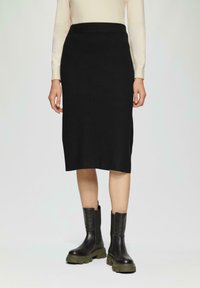 Zwarte geribde midi-rok met een aansluitende tailleband, gecombineerd met chunky zwarte leren enkellaarsjes met een olijfgroene zool.