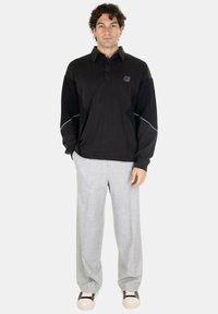 Polo shirt nero a maniche lunghe con colletto a bottoni, maniche testurizzate e dettagli bianchi, abbinato a pantaloni grigi chiari a gamba larga.