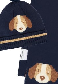 Ensemble bonnet et écharpe en tricot marine avec un design de tête de chien. Le bonnet a un pompon et une bande rayée ; l'écharpe présente un motif de chien similaire.