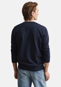 Mørkeblå sweatshirt med ribstrikkede manchetter og kant, der har en rund halsudskæring og blød tekstur, båret med lyseblå jeans. Set bagfra.