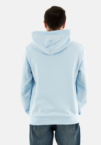 Sudadera con capucha de color azul claro, hecha de una mezcla de algodón, con cordones en la capucha y puños de canalé, combinada con jeans de mezclilla.