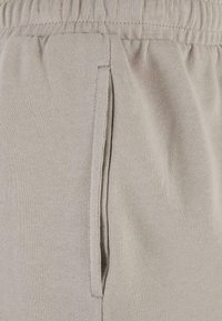 Gros plan sur un pantalon de jogging en tissu beige montrant la ceinture élastique et le détail de la poche latérale.