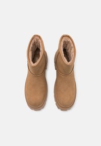 Bottes marron mi-mollet avec une finition en daim, doublure en fausse fourrure pelucheuse, bout arrondi et semelle en caoutchouc texturée, présentant une silhouette simple.