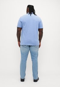 Lichtblauwe polo met korte mouwen en een kraag, gecombineerd met lichtblauwe jeans en zwarte schoenen. Gestructureerde stof, eenvoudig ontwerp.