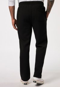Zwarte sweatpants met een elastische tailleband en achterzak, gemaakt van een gladde, zachte stof. Gecombineerd met casual witte sneakers.