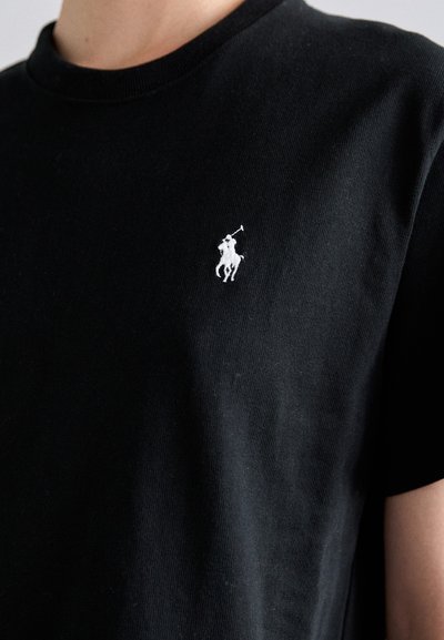 Musta puuvillapaita klassisella pyöreällä kauluksella. Vasemmassa rinnassa pieni valkoinen brodeerattu poloilijan logo.