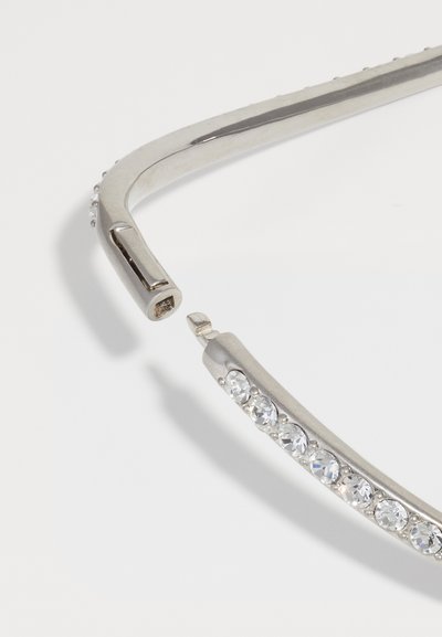 Cadran de ochelari de soare argintie cu un design curbat, prezentând un rând de cristale transparente pe lateral, textură netedă și finisaj metalic.