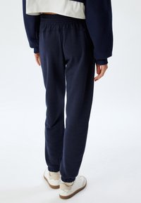Marineblauwe sweatpants gemaakt van zachte stof, met een elastische tailleband en boorden, gecombineerd met witte sneakers en een cropped top.