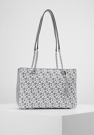 Rechteckige Handtasche mit grauem und weißem geometrischem Muster, silberne Kettenriemen mit Leder-Schulterpolstern, auf einer weißen Ausstellungsfläche.