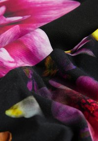 Tela con un patrón floral en tonos rosados y amarillos sobre un fondo negro. La tela parece suave y cae con naturalidad.