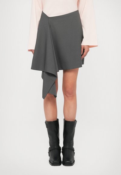 Gray mini skirt with asymmetrical hemline, made from textured fabric. Paired with black knee-high boots featuring buckles.