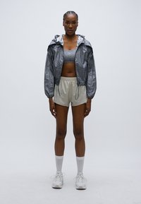 Γκρι ανακλαστικό μπουφάν με κουκούλα, συνδυασμένο με γκρι αθλητικό μπουστάκι και μπεζ σορτς. Το μοντέλο φοράει λευκά αθλητικά παπούτσια και λευκές κάλτσες μέχρι το γόνατο.