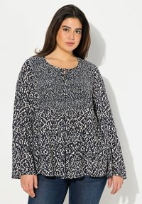 Blouse à motif bleu marine et crème avec des manches longues, un col rond et un détail en trou de serrure à l'avant. Tissu doux et léger avec un design fluide.