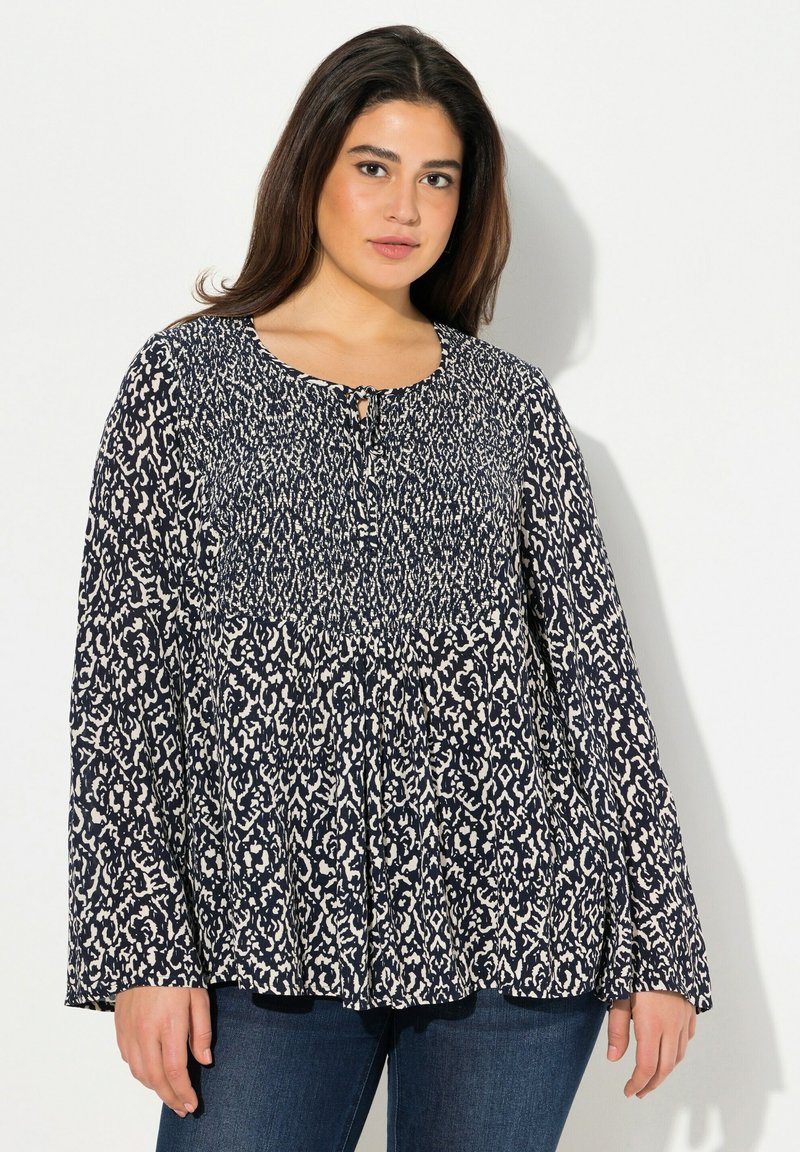 Blouse à motif bleu marine et crème avec des manches longues, un col rond et un détail en trou de serrure à l'avant. Tissu doux et léger avec un design fluide.